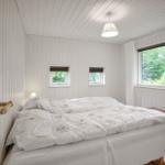 Schlafzimmer mit Bett, zwei Fenstern und Poster an der Wand.