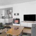 Dining area with table and chairs, kitchen in background, fireplace in living area.