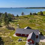 Rotes Haus mit Terrasse, umgeben von Wald und Meer.