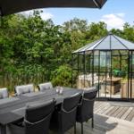 Terrasse mit Tisch, zwei Gläsern und einer Flasche Wein. Hintergrund: Glaswand und grüne Pflanzen.