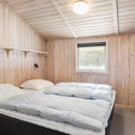 Schlafzimmer mit Holzwand, Bett und Fensterblick auf Wald.