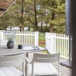 Terrasse mit Tisch, Stühlen und Pflanzen hinter weißem Zaun.