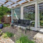 Haus mit großem Glasbereich und Garten mit Blumenbeeten und Pergola.