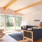 Wohnraum mit Sofa, Sessel und Kaminofen. Holzwände und -boden. Fenster mit Blick auf Außenbereich.