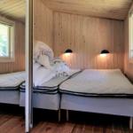 Schlafzimmer mit Holzwand, Bett und Fenster mit Jalousie.