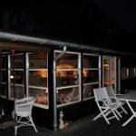 Schwarze Holzhütte mit Terrasse und Schneelandschaft unter Bäumen