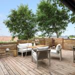 Terrasse mit Sitzgruppe, Tisch und Pflanzen. Holzdecke und Zaun. Blick auf Landschaft.