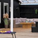 Terrasse mit Sitzgruppe, Holztisch und Pflanzen vor schwarzem Holzhaus