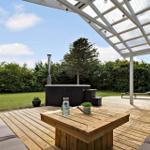 Terrasse mit Holztisch, Sitzgelegenheiten und Whirlpool unter einer Glasdachkonstruktion.