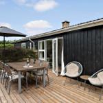 Terrasse mit Tisch, Stühlen und Sonnenschirm neben einem Haus mit Schiebetür.