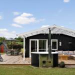 Schwarzes Holzhaus mit Terrasse, Whirlpool und Sitzgelegenheiten im Garten.