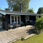 Deck with table, chairs, and red umbrella. Grill and trampoline in the garden.