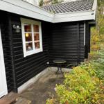 A black wood stove with a burning fire is against a stone wall and wooden ceiling.