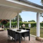 Moderne Villa mit großem Balkon und Garten. Terrasse mit Sitzgelegenheiten und Blick auf Bäume.