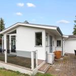 Moderne Villa mit überdachtem Balkon und großem Garten. Holzterrasse und Bäume umgeben das Haus.