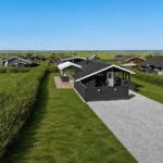 Schwarze Holzhütte mit Terrasse, umgeben von Gras und Hecken. Blick auf das Meer.