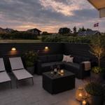Terrasse mit Sitzgruppe, Liegestühlen und Beleuchtung. Blick auf Wohngebiet mit dänischer Flagge.