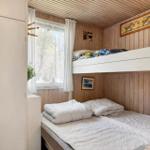 Schlafzimmer mit Doppelbett und obere Schlafcouch. Holzwände und Fenster mit weißen Vorhängen.