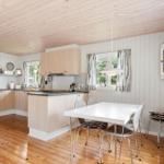 Kitchen with dining area, wooden floor, and light walls. White furniture and windows with striped curtains.