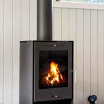 A wood-burning stove stands against a wall with vertical panels. Two glasses sit on a table.