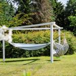 Two hammocks under a white frame in the garden with grass and trees.