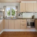 Kitchen with wooden cabinets, stainless steel oven, and windows to the garden.