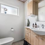Bathroom with toilet, sink, and wooden cabinets. Window with plant.
