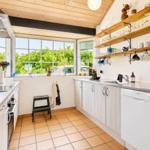 Küche mit Holzdecke, Fenstern zum Garten und Küchenzeile mit Spüle und Waschmaschine.