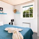 Schlafzimmer mit blauem Bett, Fenster und weißen Wänden.
