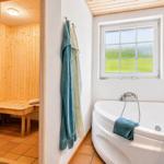 Badezimmer mit Badewanne und Sauna. Fenster mit grünem Blick. Handtücher an der Wand.