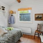 Schlafzimmer mit Bett, Wandleuchte und Fenster. Holzwände und ein Stuhl sind sichtbar.