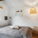 Schlafzimmer mit Bett, Wickerstuhl und Wandbild. Holzwand und Dachschräge.