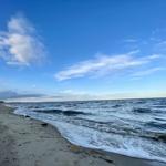 Weiterer Blick auf den Strand mit Dünen und blauem Himmel.
