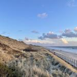 Wellen brechen auf dem Strand. Horizont mit blauem Himmel und weißen Wolken.