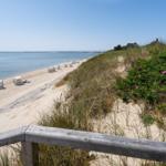 Strand mit Sand, Meer und Strandkörben. Im Hintergrund steht ein Gebäude.
