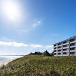 Strand mit Sandkörben und Dünenvegetation. Holzsteg führt zum Strand.