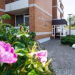 Holzweg durch grüne Hecken mit rosa Blumen zum Meer