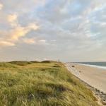 Strand mit Sand, Strandkörben und Holzsteg unter blauem Himmel.