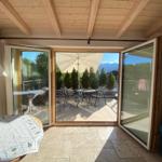 Terrasse mit Tisch, Stühlen und Sonnenschirm. Durchgehende Glasschiebetüren führen ins Freie.