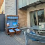 Terrasse mit Strandkorb, Tisch und Bänken. Modernes Haus mit Holz- und Steinverkleidung.