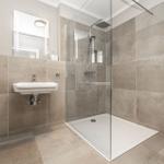 Badezimmer mit Dusche, Waschbecken und Toilette. Fliesenwand und Boden.