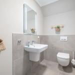 Badezimmer mit Waschbecken, Spiegel und Toilette. Wandhalterungen und Körbe sind sichtbar.