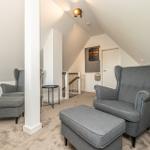 Zwei graue Sessel mit Füßen und Fußhocker im Dachgeschoss mit schrägen Wänden und Treppe.