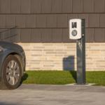 Elektrischer Ladeplatz für Autos vor einem Gebäude mit Steinmauer und Gras.