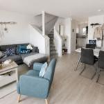 Wohn- und Essbereich mit Sofa, Sessel und Tisch. Treppenhaus führt zur oberen Etage.