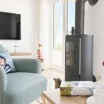 Ein Wohnzimmer mit Sofa, Kaminofen und Fernseher. Auf dem Tisch steht eine Tasse und ein Buch.