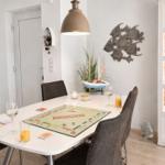 Esszimmer mit Tisch, Stühlen und Monopoly-Spiel. Wanddekoration und Getränkeflaschen sichtbar.
