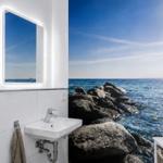 Badezimmer mit Meeresmotiv-Wand, Waschbecken und beleuchtetem Spiegel.