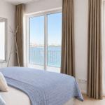 Schlafzimmer mit Blick aufs Wasser und Balkon. Bett, Spiegel und Gardinen sind sichtbar.