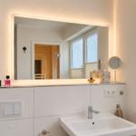 Badezimmer mit beleuchtetem Spiegel, Waschbecken und Fenster.